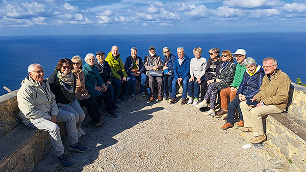 Reisegruppe mit 16 Teilnehmer sitzend im Halbkreis auf einer Steinmauer - im Hintergrund das tiefblaue Mittelmeer