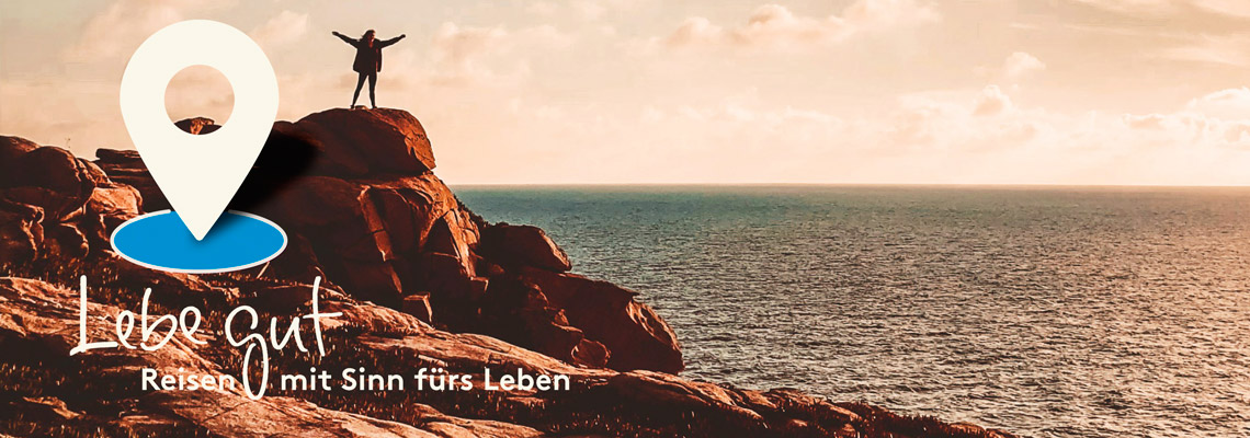 Ein Mann steht auf einem Felsen am Meer mit ausgebreiteten Armen